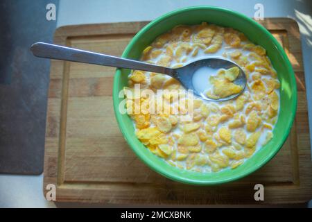 Corn flakes with milk in a green bowl with a spoon, top view Stock Photo