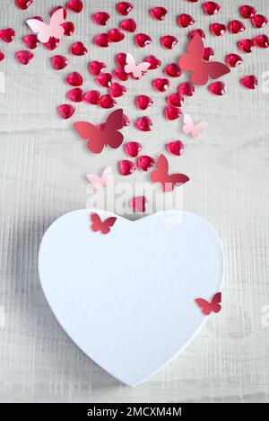 White heart shaped gift box with red hearts and butterfly on grey background. Design for Valentine's Day. Stock Photo