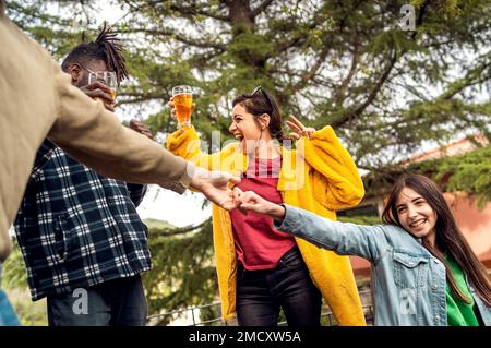 A group of multiethnic friends enjoy a festive and joyful moment in a countryside pub or beer garden, dancing on tables and drinking beer from mugs. T Stock Photo