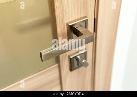 Modern chrome metal door handle on wooden door. Stock Photo