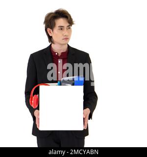 Young Asian businessman in black suit showing absent-minded, stressed and unhappy expression, holding paper box of belongings collected from office in Stock Photo