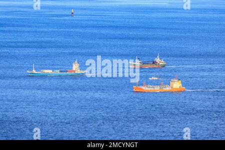 Small Fleet of Cargo Ships Sail through Shipping Lane in Calm Blue Sea Stock Photo