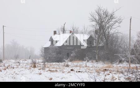 An old black and white abandoned haunted spooky looking farmhouse in winter on a farm yard in rural Ontario, Canada Stock Photo