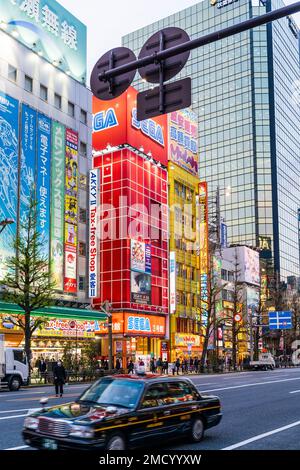 View along Chuo Dori, the main shopping street in Akihabara, Tokyo. Buildings illuminated, taxi in the foreground and the Sega Red building behind. Stock Photo