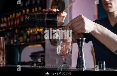 Barkeeper pouring ready pink smoothie cocktail Bartender makes a cocktail from the bar counter. Bar nightlife atmosphere Stock Photo