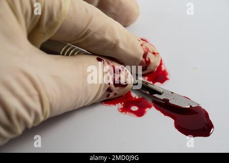 blood stained sterile stainless steel blade and latex glove health professional surgeons scalpel isolated on a white background with pool of blood Stock Photo