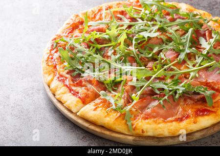 Classic Italian Pizza Prosciutto with tomato sauce, mozzarella, ham, arugula close-up on a wooden board on the table. Horizontal Stock Photo