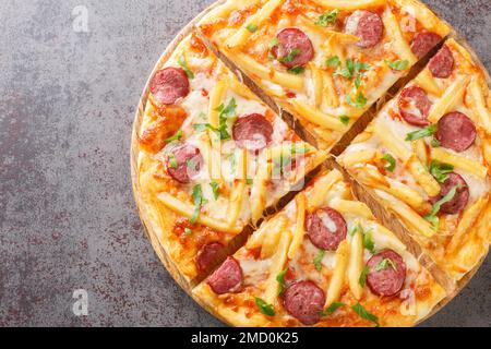 Americana Pizza with french fries, wurstel sausages, mozzarella cheese, tomato sauce and herbs close-up on a wooden board on the table. Horizontal top Stock Photo