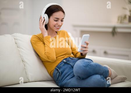 Positive young lady using headphones and cell phone at home Stock Photo