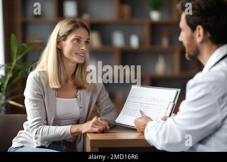 Smiling Doctor Man Discussing Medical Test Results With Female Patient In Clinic Stock Photo
