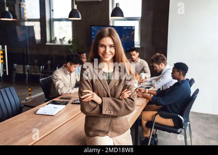 Happy caucasian businesswoman posing standing with folded arms in modern office during corporate meeting Stock Photo