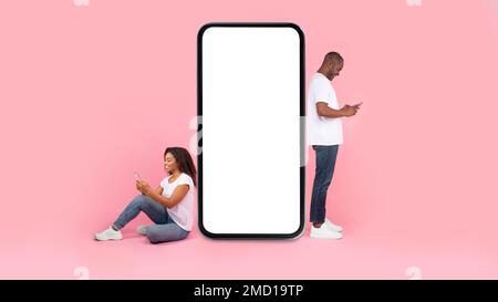 Cool application. Black couple near giant smartphone with blank white screen using gadgets, mock up, full body length Stock Photo