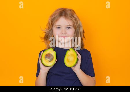 Kid hold red avocado in studio. Studio portrait of cute child with avocado isolated on yellow background, copy space Stock Photo