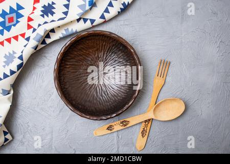 Vintage wooden bowl with wood cutlery and ethnic patterned cloth on gray cement background Stock Photo