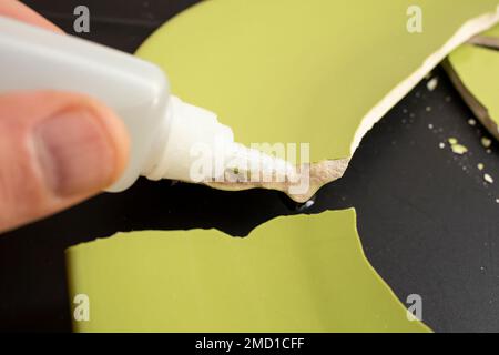 Hand applying liquid glue on ceramic broken pieces, repairing a green plate, soft focus close up Stock Photo