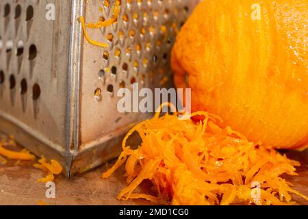 Orange zest and vintage grater on a wood chopping board, soft focus close up