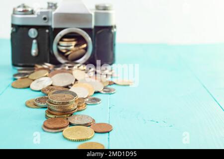 Defocused vintage camera with coins on the foreground, on blue background, soft focus close up Stock Photo