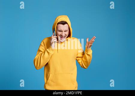 angry man in yellow sweatshirt holding mobile phone Stock Photo