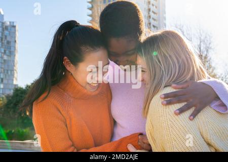 Three female friends affectionately hug each other having fun together laughing happy smiling.  Stock Photo