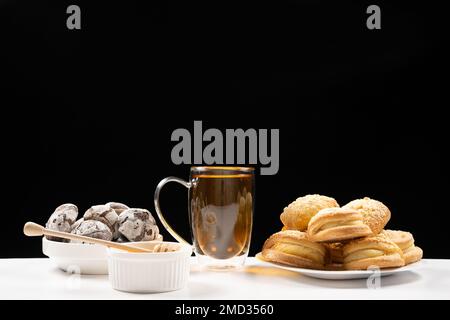 Tea with honey with cocoa cookies and cakes with creamy filling on a black background. Stock Photo