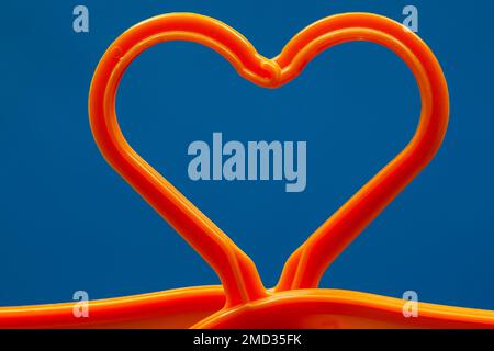 A heart for clothes. Two orange plastic hangers on a blue background that combine to form a heart shape. Stock Photo