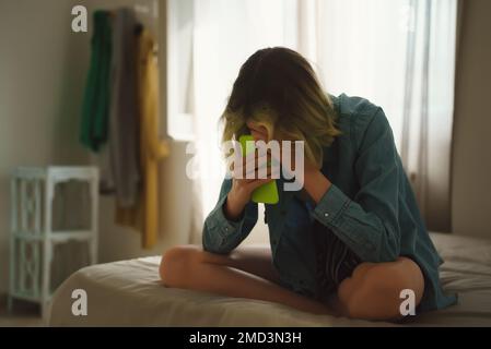Upset teen girl on bed with phone. Stock Photo