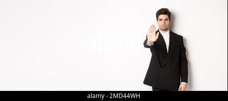 Portrait of serious handsome man in formal suit, extending hand to stop you, prohibit action, forbid and disagree with something, standing against Stock Photo