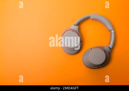 Light gray wireless over-ear headphones on an orange background. Headphones for playing games or listening to music. Noise canceling headphones. Top v Stock Photo