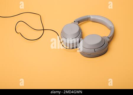 Light gray wireless on-ear headphones with the ability to connect via wire on a peach background. Headphones for playing games or listening to music. Stock Photo