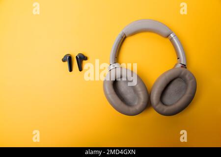 Light gray wireless on-ear headphones and blue in-ear wireless headphones on a yellow background. Comparison of different types of headphones. Headpho Stock Photo