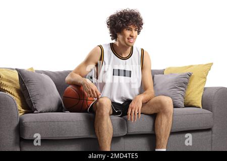 Guy in a sports jersey with a baskteball sitting on a sofa isolated on white background Stock Photo