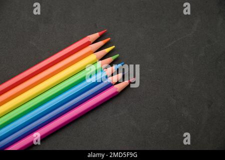 Background for school or artistic content where some colored pencils appear on a textured black surface. Image with copy space. Stock Photo