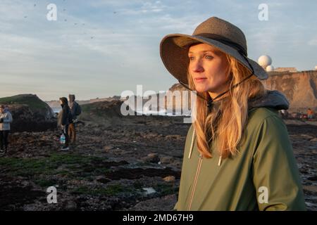 A blonde woman in the evening light looking out to the distance at low tide on the California seashore. Stock Photo