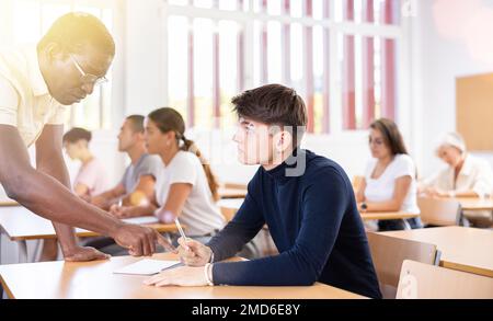 Professor explaining task solution to young man in college Stock Photo