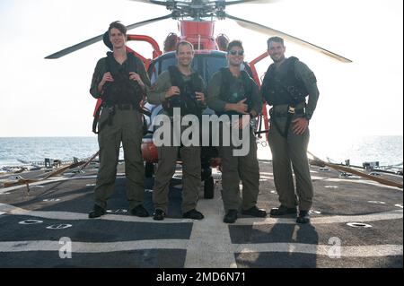 Flight crew members of an U.S. Coast Guard MH-65 Dolphin, an asset from Coast Guard’s Helicopter Interdiction Tactical Squadron (HITRON), pose for a group photo in between deck landing qualification exercises, Atlantic Ocean, July 13, 2022. Deck landing qualifications allow for both the boat and air crews to successfully train personnel in landing a helicopter on board a vessel. Stock Photo