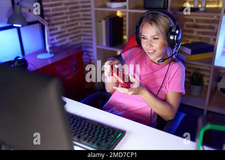 Young blonde woman streamer playing video game using joystick at gaming room Stock Photo