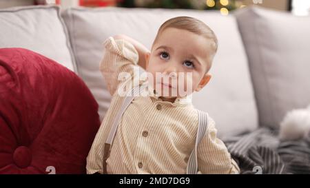 Adorable toddler standing by christmas tree with serious expression at home Stock Photo