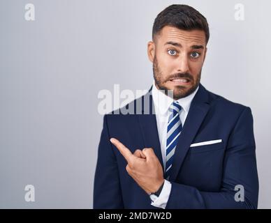 Handsome hispanic man wearing suit and tie pointing aside worried and nervous with forefinger, concerned and surprised expression Stock Photo