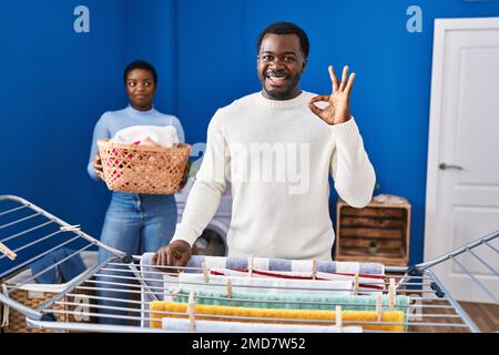 Young african american couple hanging clothes at clothesline doing ok sign with fingers, smiling friendly gesturing excellent symbol Stock Photo