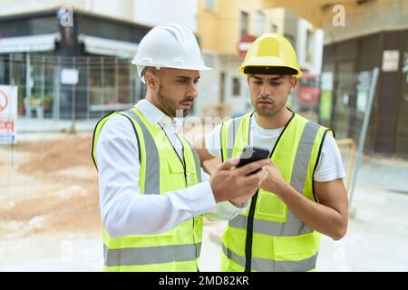 Two hispanic men architects using smartphone standing at street Stock Photo