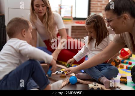 Teachers with boy and girl playing with cars toy sitting on floor at ...