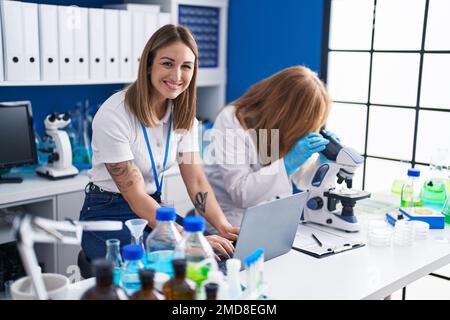 Mother and daughter scientists using laptop and microscope at laboratory Stock Photo
