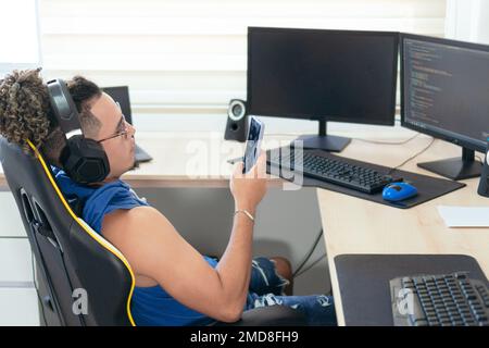 Computer programmer sitting in his office and typing on his cell phone. Stock Photo