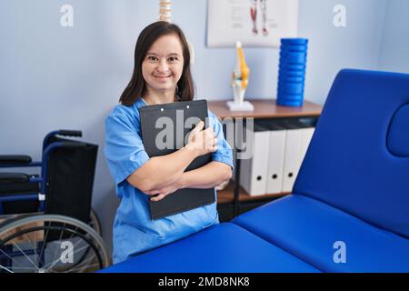 Down syndrome woman wearing physiotherapy uniform holding clipboard at physiotherapist clinic Stock Photo