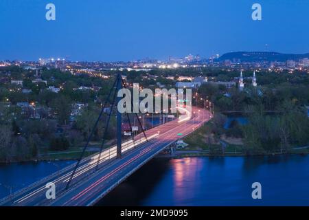 View of Papineau bridge over Riviere des Prairies with downtown Montreal skyline and Mont-Royal in the distance at dusk., Quebec, Canada. Stock Photo
