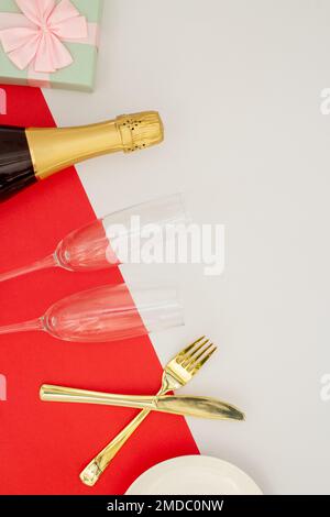 Festive table set concept, Champagne with glass and cutlery with gift box on red white background. Stock Photo