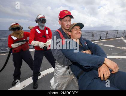 PHILIPPINE SEA (July 15, 2022) Gas Turbine Systems Technician (Mechanical) 2nd Class Austin Lynch, from Temple, Texas, carries a simulated casualty, Quartermaster 3rd Class Brandon Gonzalez, from Boise, Idaho, during a firefighting drill on the flight deck aboard Arleigh Burke-class guided-missile destroyer USS Benfold (DDG 65). Benfold is assigned to Commander, Task Force (CTF) 71/Destroyer Squadron (DESRON) 15, the Navy’s largest forward-deployed DESRON and the U.S. 7th Fleet’s principal surface force. Stock Photo