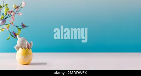 A white rabbit hid in an Easter egg on a blue background. Festive Easter card. Copy space.  Stock Photo