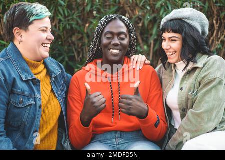 Three young women, an African woman with dreadlocks, a curvy woman with non-binary gender, and a brunette, are seen spending time together chatting an Stock Photo