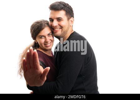 Cute smiling female model making stop stay away gesture using palm while hugging male boyfriend as romantic couple relationship concept isolated on wh Stock Photo